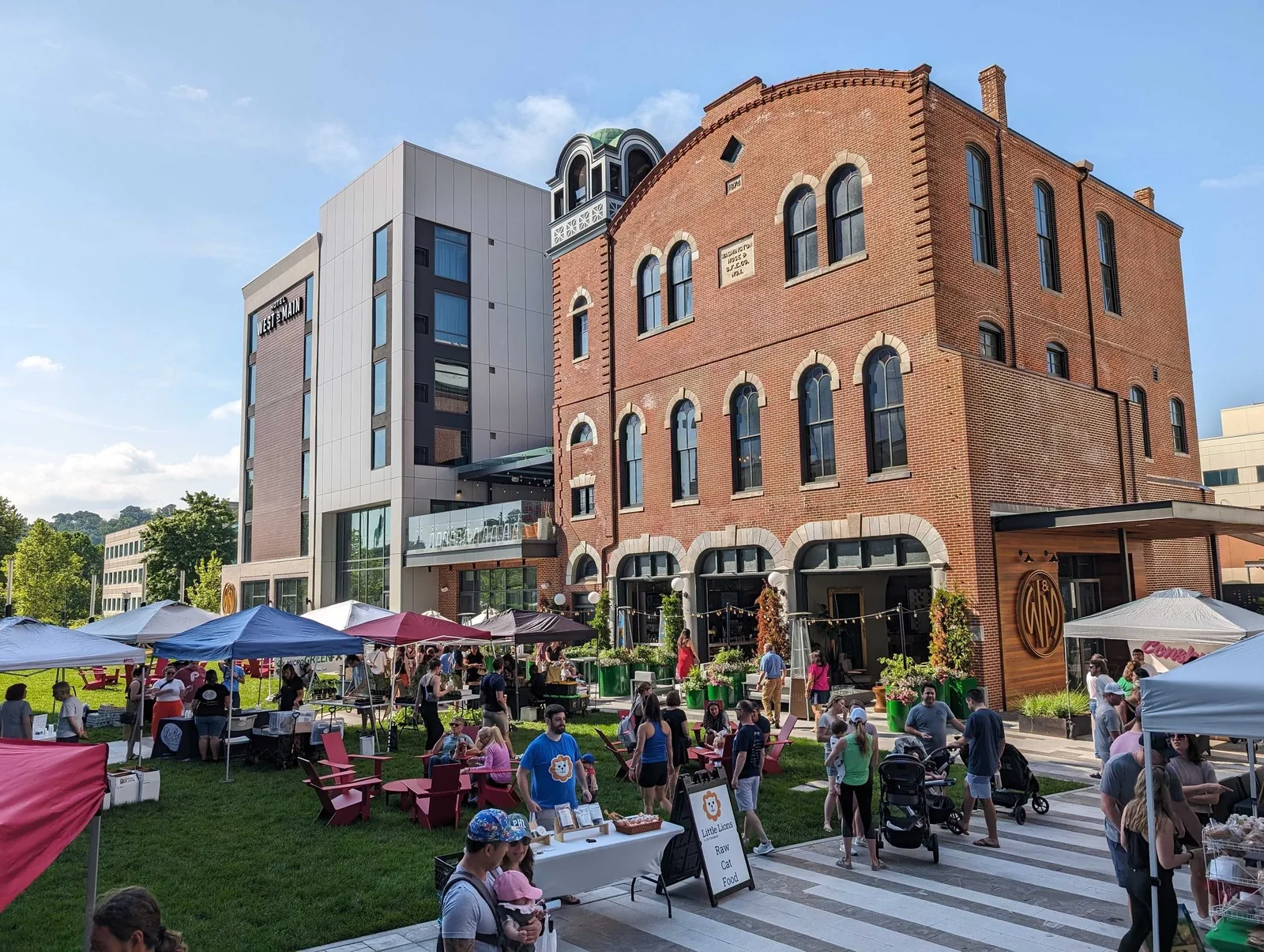 People browse tents at a farmers market beside downtown Conshohocken buildings.